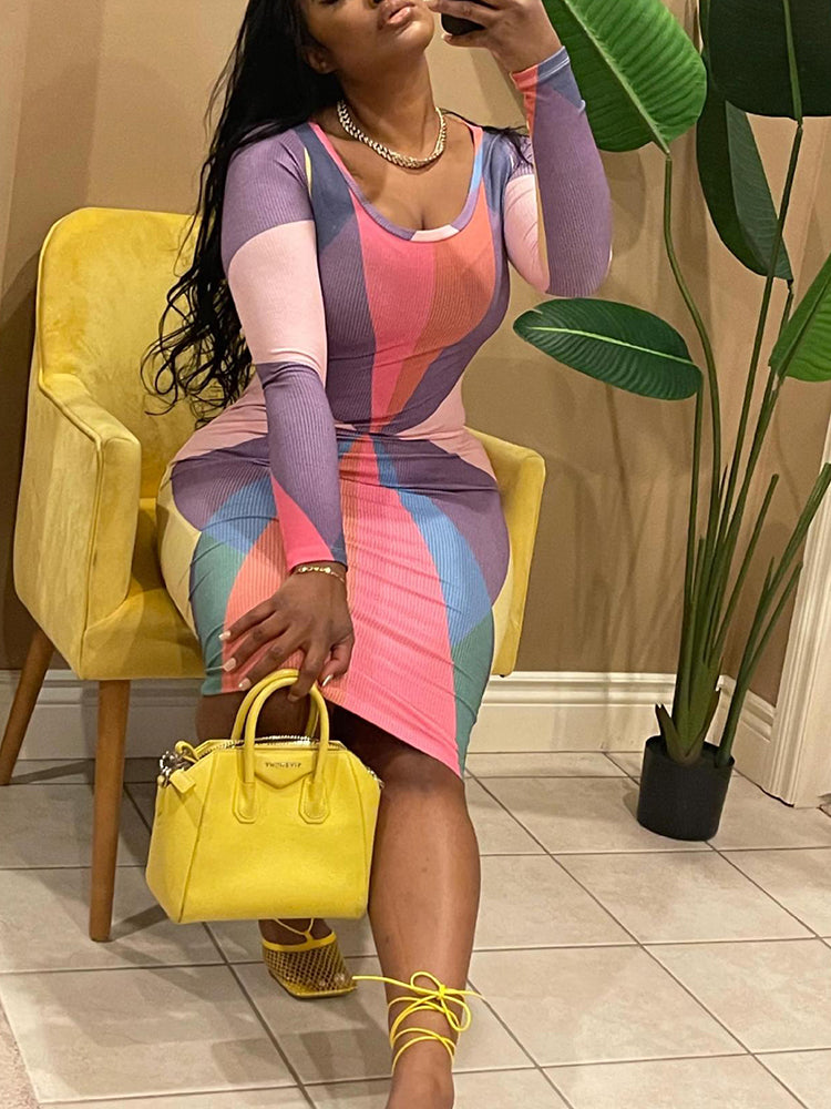Woman sitting on a yellow chair, wearing a long-sleeved, multi-colored geometric print bodycon dress, holding a yellow handbag.