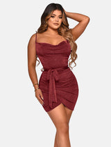 Woman wearing a short burgundy sparkly dress with a cowl neckline and spaghetti straps, tied at the waist with a matching belt, against a white background.