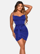 Woman wearing a short royal blue sparkly dress with a cowl neckline and spaghetti straps, tied at the waist with a matching belt, against a white background.