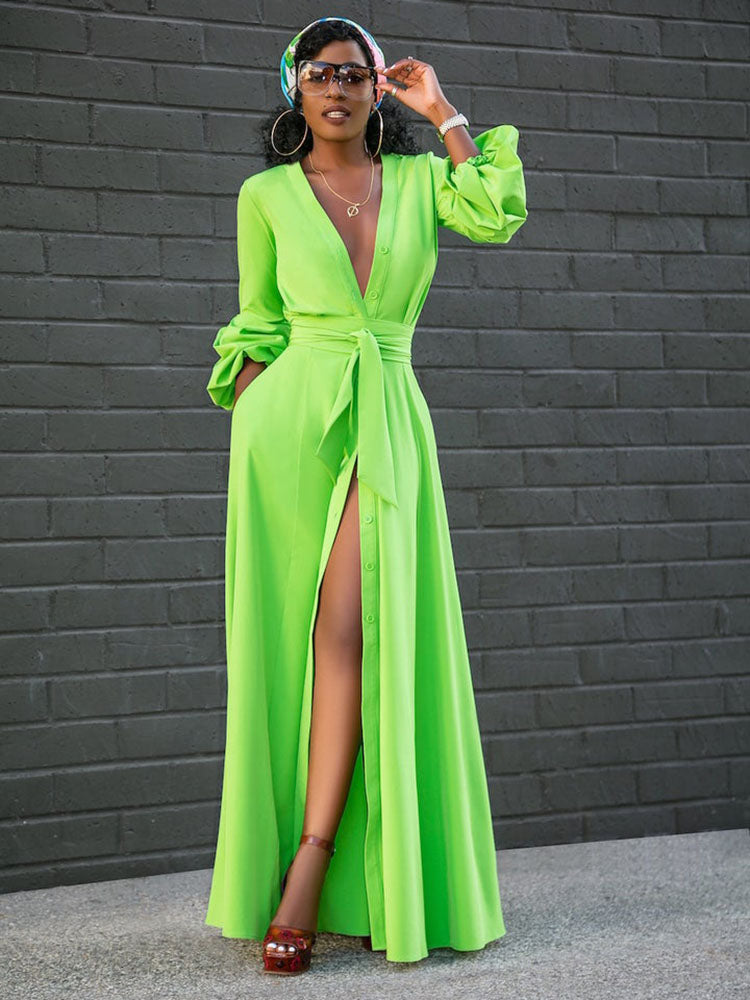 Woman wearing a vibrant lime green long sleeve maxi dress with a deep V-neck, button-down front, self-tie belt, and a high slit, accessorized with a headscarf and sunglasses.