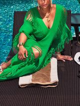 Woman relaxing by a pool in a green distressed knit maxi dress with fringe detailing.