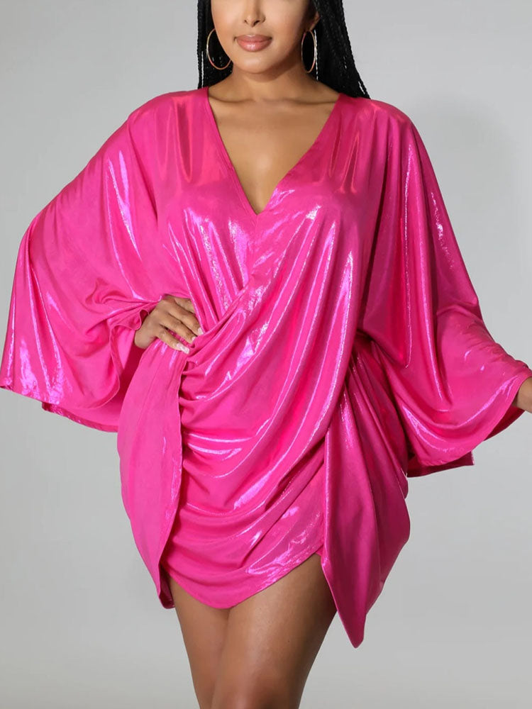Full body shot of a woman in a vibrant pink metallic dress with wide sleeves.