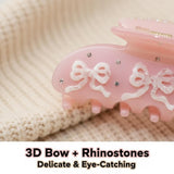 Close-up of a pink hair claw clip featuring 3D bows and rhinestones, with text overlay '3D Bow + Rhinestones Delicate & Eye-Catching'