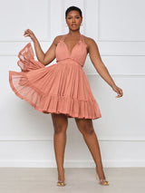 Woman in a coral pink halter neck mini dress with a deep V-neckline and tiered ruffled skirt, twirling to show the movement of the skirt.