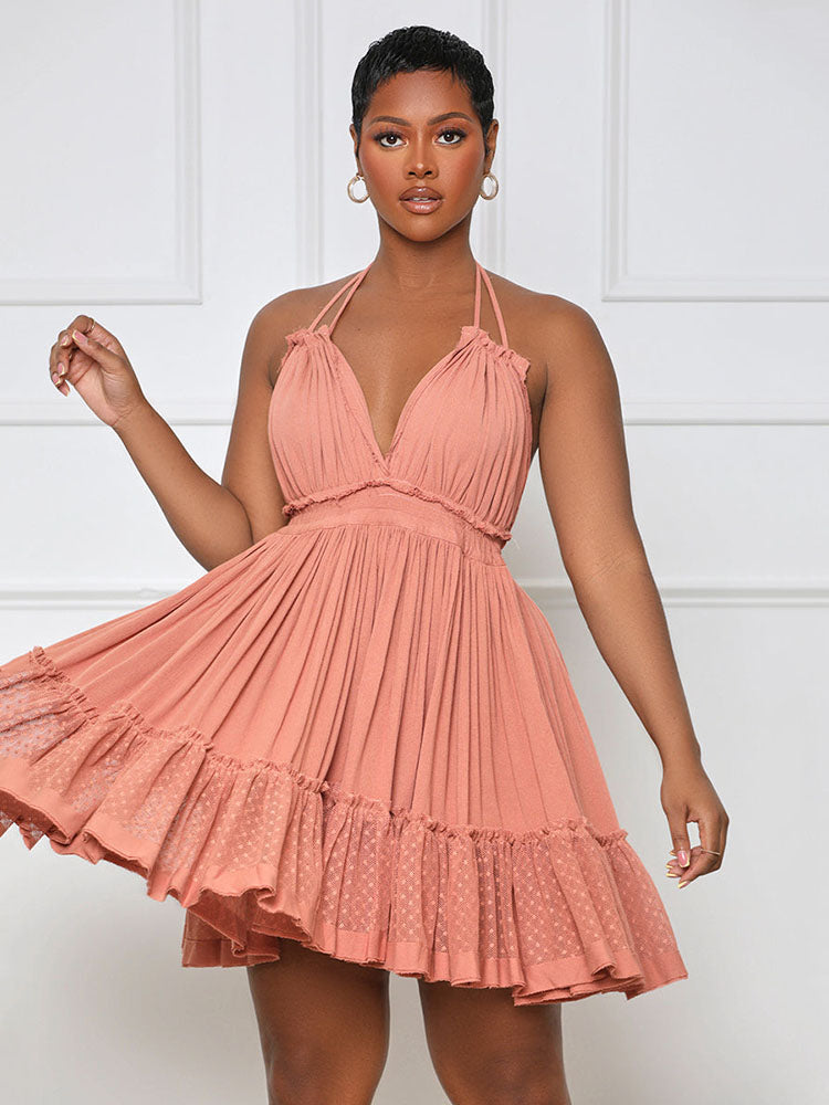 Close-up of a woman in a coral pink halter neck mini dress with a deep V-neckline and tiered ruffled skirt, her arm extended.