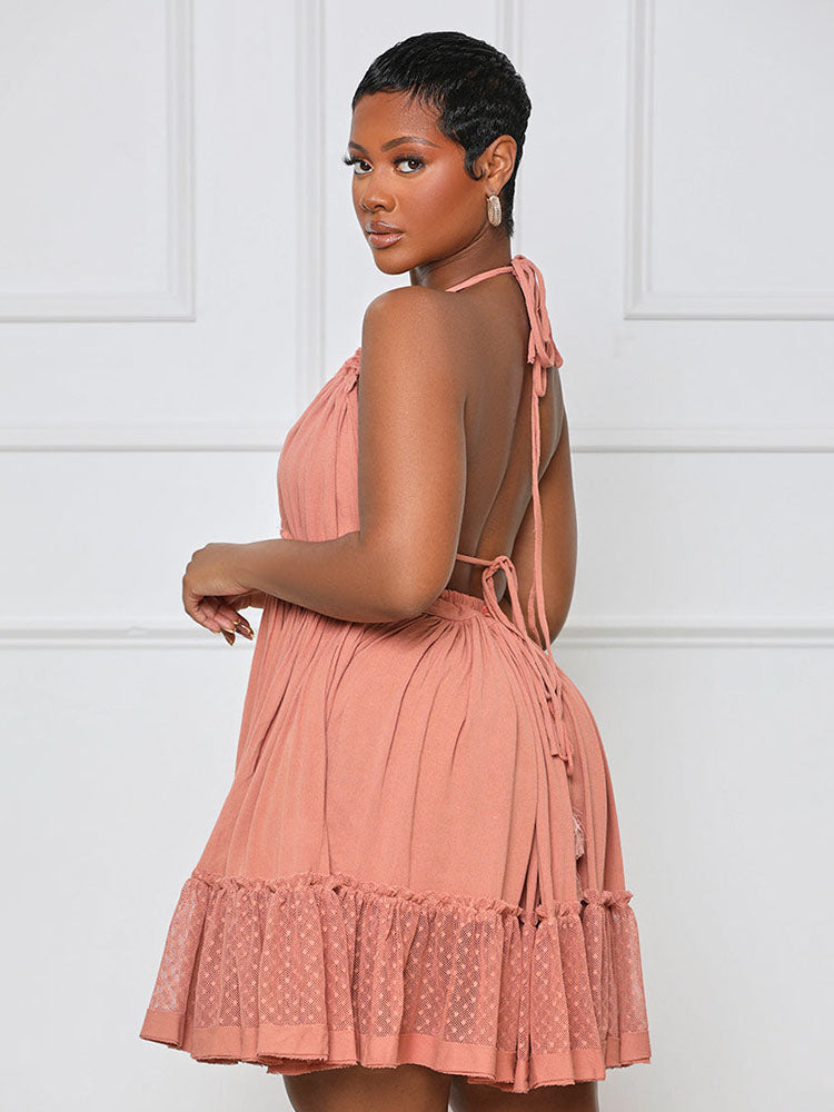 Rear view of a woman wearing a coral pink halter neck mini dress with an open back and tie detail, showing the tiered ruffled skirt.