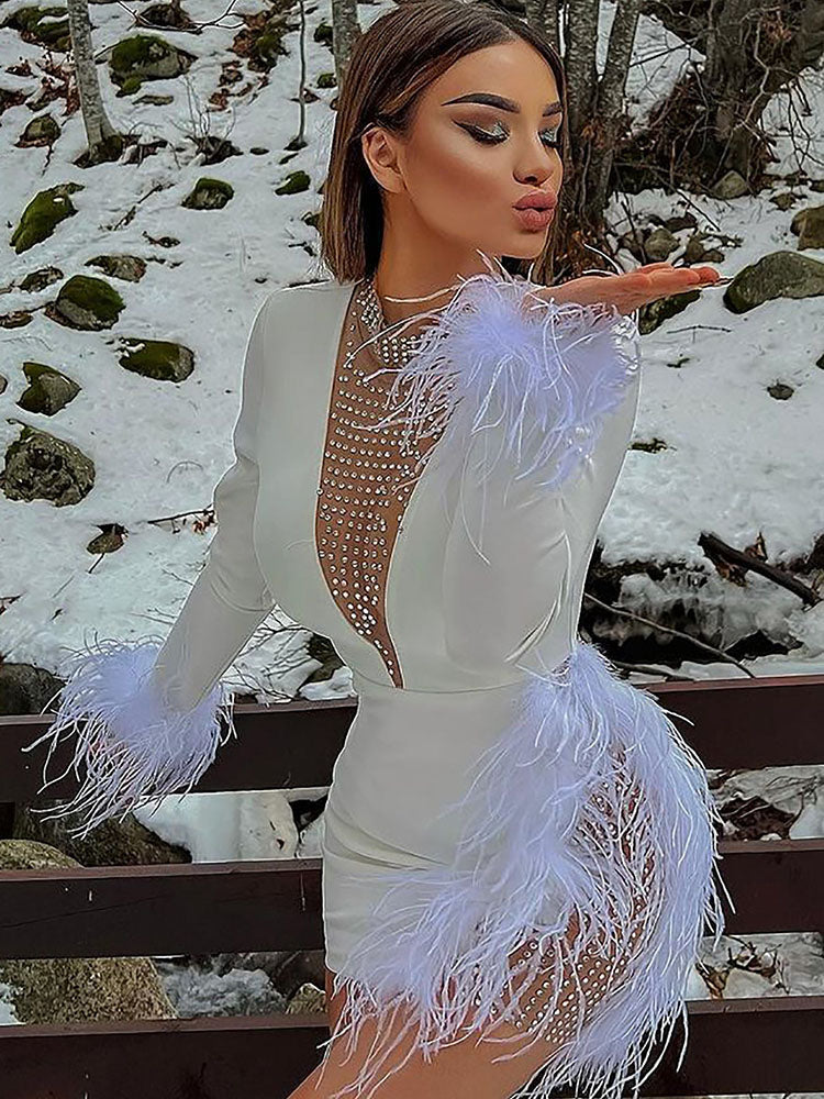 Woman in a white long-sleeved bodycon mini dress with feather trim on the sleeves and side cutout, adorned with crystal embellishments on the neckline and cutout, posing outdoors.