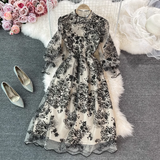 Elegant black and white floral embroidered midi dress with sheer puff sleeves and sequin details, shown on a hanger with a white faux fur rug and silver heels.