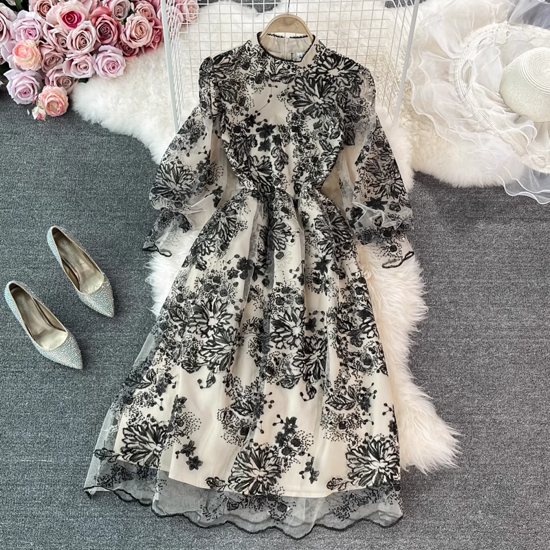 Elegant black and white floral embroidered midi dress with sheer puff sleeves and sequin details, shown on a hanger with a white faux fur rug and silver heels.