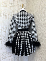 Back view of a black and white houndstooth knit dress with feather trim cuffs and a pleated skirt on a mannequin.