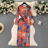 A long-sleeved, abstract print maxi dress with a side slit is laid flat on a white faux fur rug.