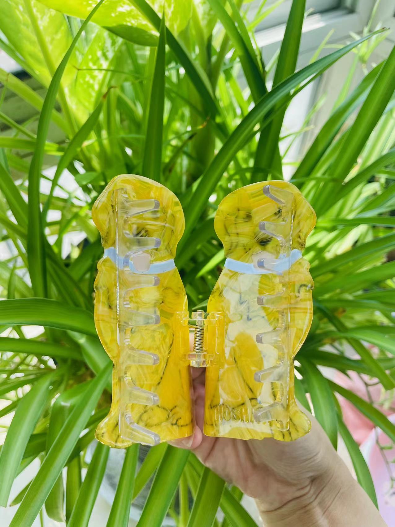 Two yellow marbled acrylic dog-shaped hair clips held by hand
