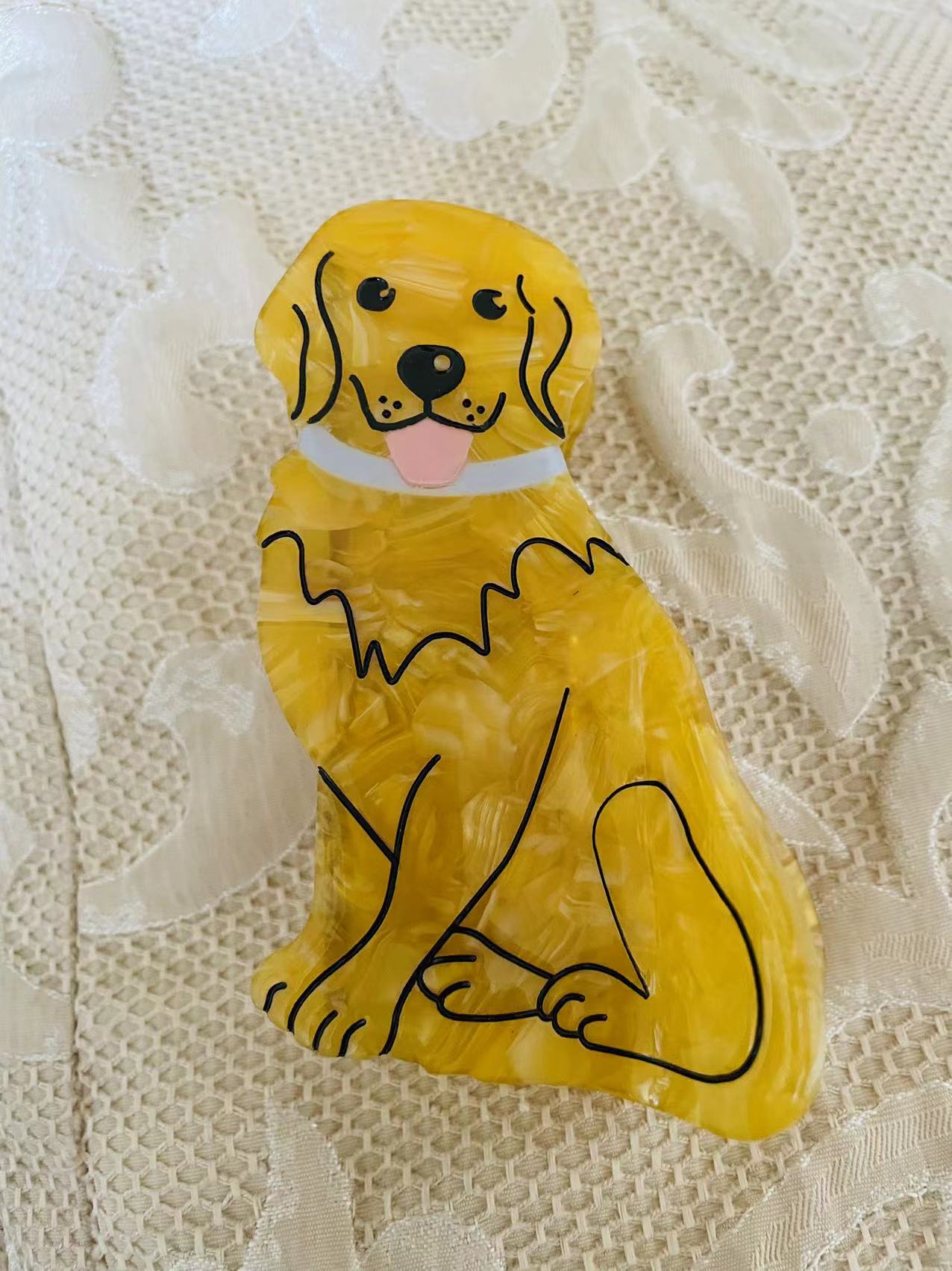 Front view of a yellow marbled acrylic dog-shaped hair clip on a textured background