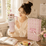 Woman holding a pink and white mug with a matching gift box on a table.
