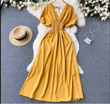 Yellow maxi dress with smocked waist and puff sleeves laid flat on a fluffy rug with a straw hat and a small beaded purse