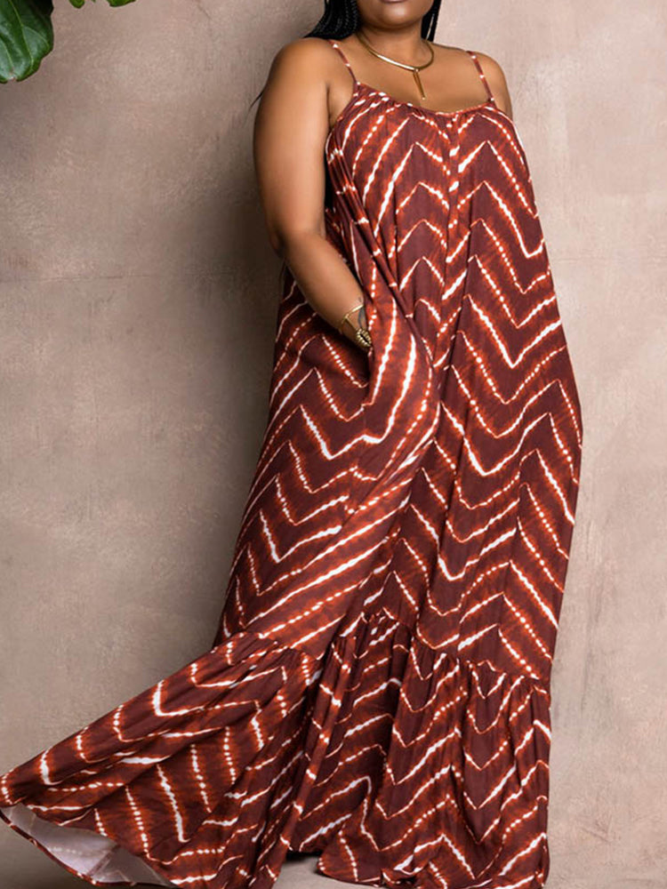 Woman wearing a brown and white tie-dye print maxi dress with spaghetti straps and a ruffled hem, standing against a textured brown wall.