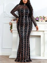 Woman in a long black dress with gold sequin embellishments, standing in front of a fireplace with flowers.