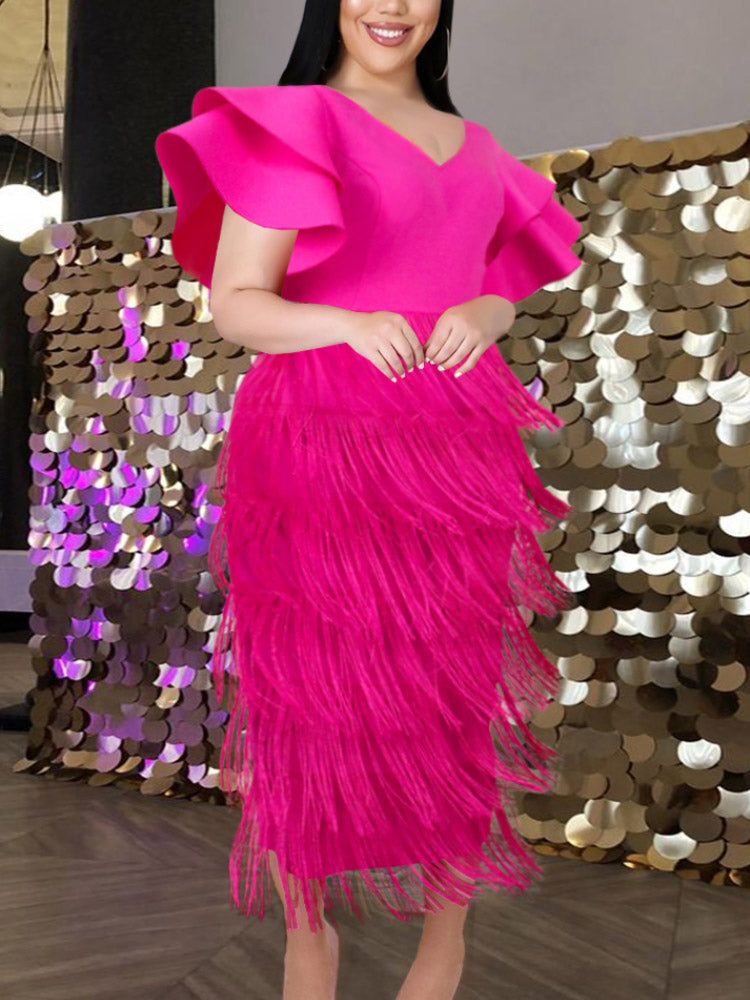 A woman in a magenta tiered fringe dress with flutter sleeves smiles, with a shimmering gold sequin backdrop.