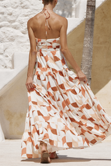 Back view of a woman wearing a halter maxi dress with a geometric print and tiered skirt, walking away.