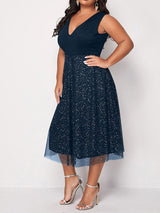 Side view of a woman in a navy blue sleeveless V-neck midi dress with sparkly embellishments and a tulle overlay.