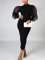 Full body shot of a woman in a black bodycon dress with voluminous sheer sleeves.