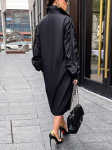 Back view of a woman wearing a black collared shirt dress with long ruffled sleeves and an asymmetrical hemline, carrying a black handbag and wearing black and gold heels.