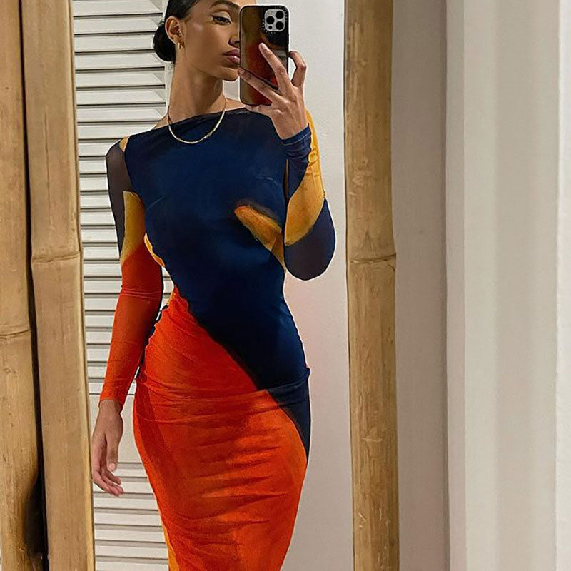 Woman taking a mirror selfie in a fitted, long-sleeve dress with an abstract orange, blue, and yellow print.