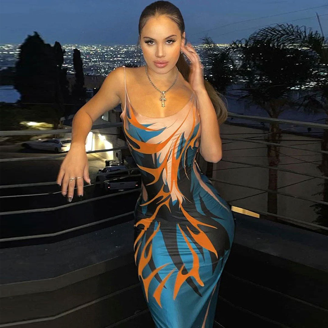 Woman in a long bodycon dress with a flame print, posing on a balcony at dusk.