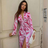 Woman wearing a pink and white abstract print long sleeve midi dress with a collared V-neck and a high slit.