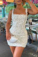 Woman wearing a white sequined mini dress and holding a white clutch bag in a restaurant setting.