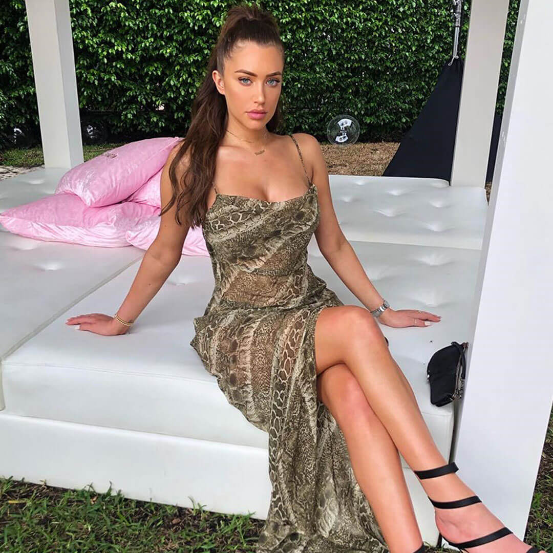 woman wearing a long snake print slip dress with a cowl neck and spaghetti straps sitting on a white outdoor daybed