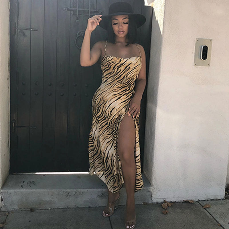 Woman wearing a tiger print slip dress with a high slit and a black hat.