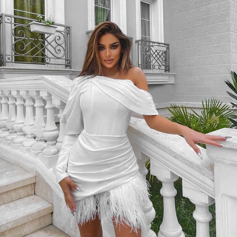Woman wearing a white asymmetrical mini dress with a feather trim hem and one long sleeve, standing on a white staircase.
