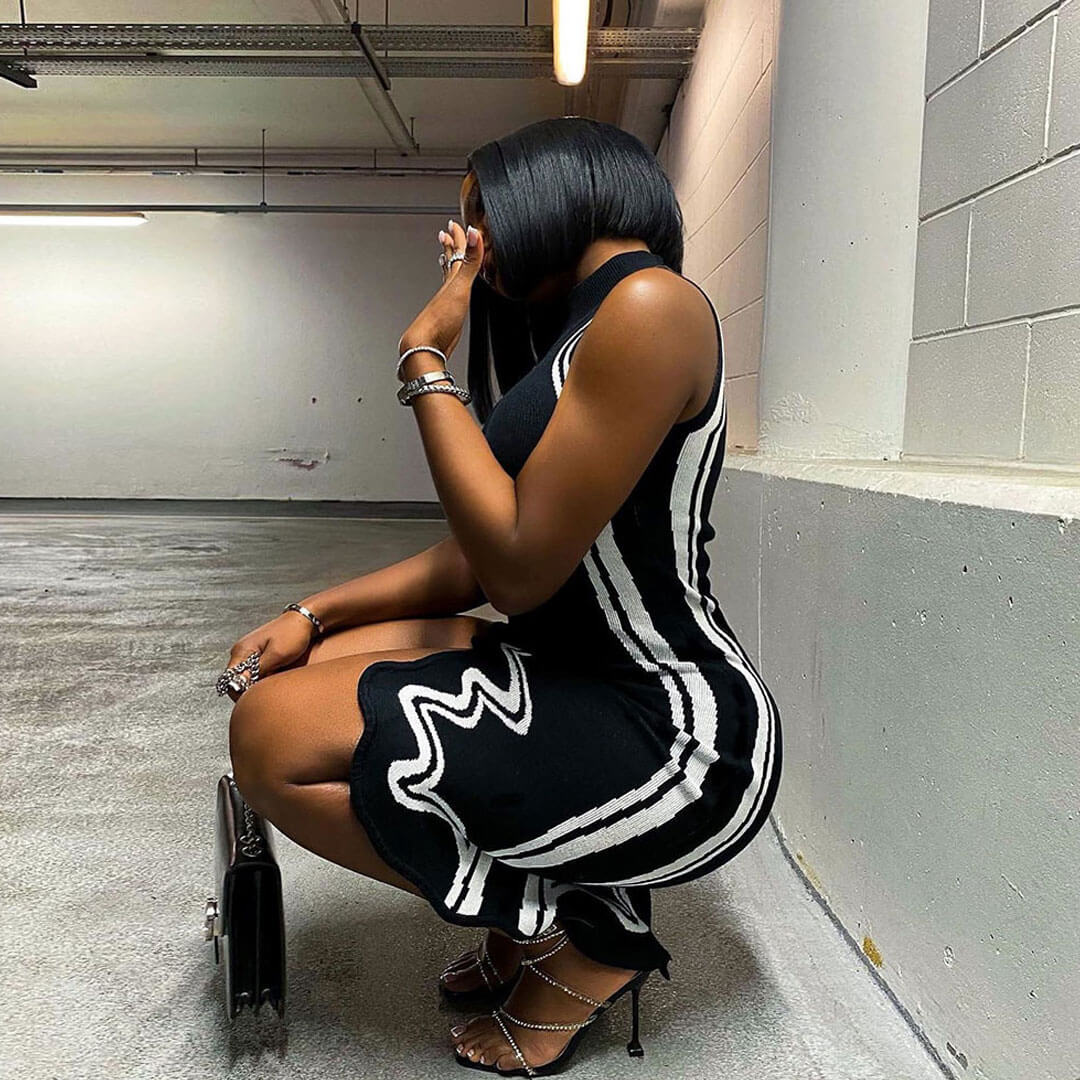 woman in black sleeveless dress with white piping and asymmetrical hem, crouching