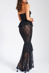 Woman wearing a black lace strapless gown with a peplum waist and tiered fishtail hem, back view