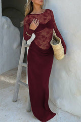 Woman wearing a long burgundy lace dress with a ruched waist and a straw bag.