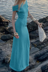 Woman wearing a turquoise off-the-shoulder maxi dress standing on rocks by the water