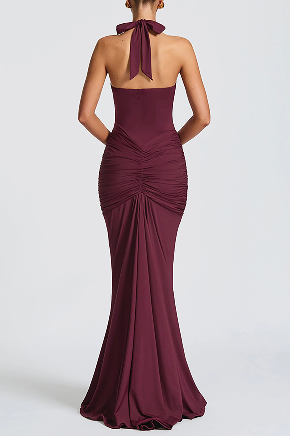 Back view of a woman wearing a burgundy floor-length halter dress with a deep V-neckline and ruched detailing.