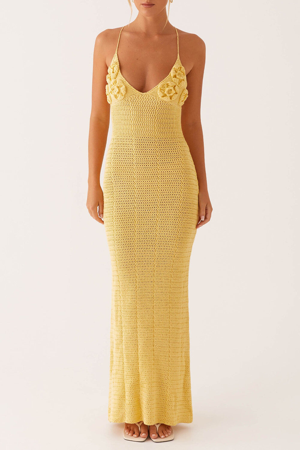 woman wearing a yellow crochet knit maxi dress with floral applique detail on the bust and a v-neckline