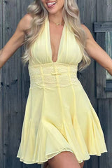 woman in a yellow halter neck mini dress with lace detailing, arms outstretched, in front of a wooden fence.