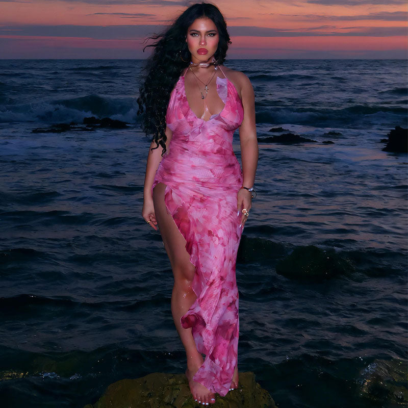 woman in pink floral print halter maxi dress standing on rock by the ocean at sunset