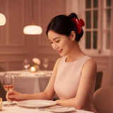 Woman with dark hair in an updo secured with a red claw clip, seated at a table with a glass of wine