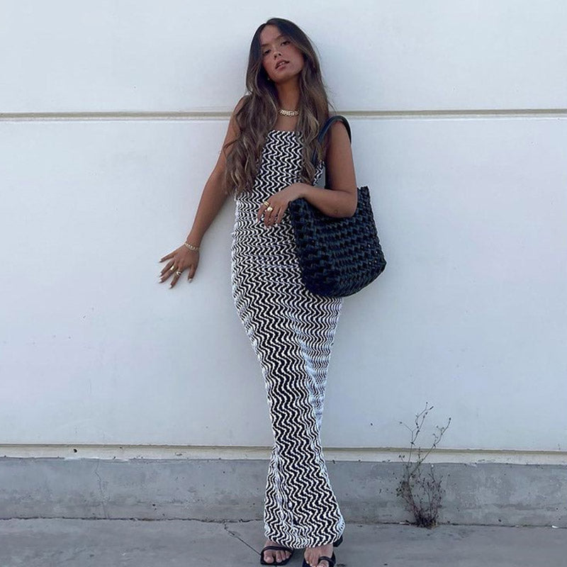 Woman leaning against a white wall wearing a black and white chevron print maxi dress and black tote bag.