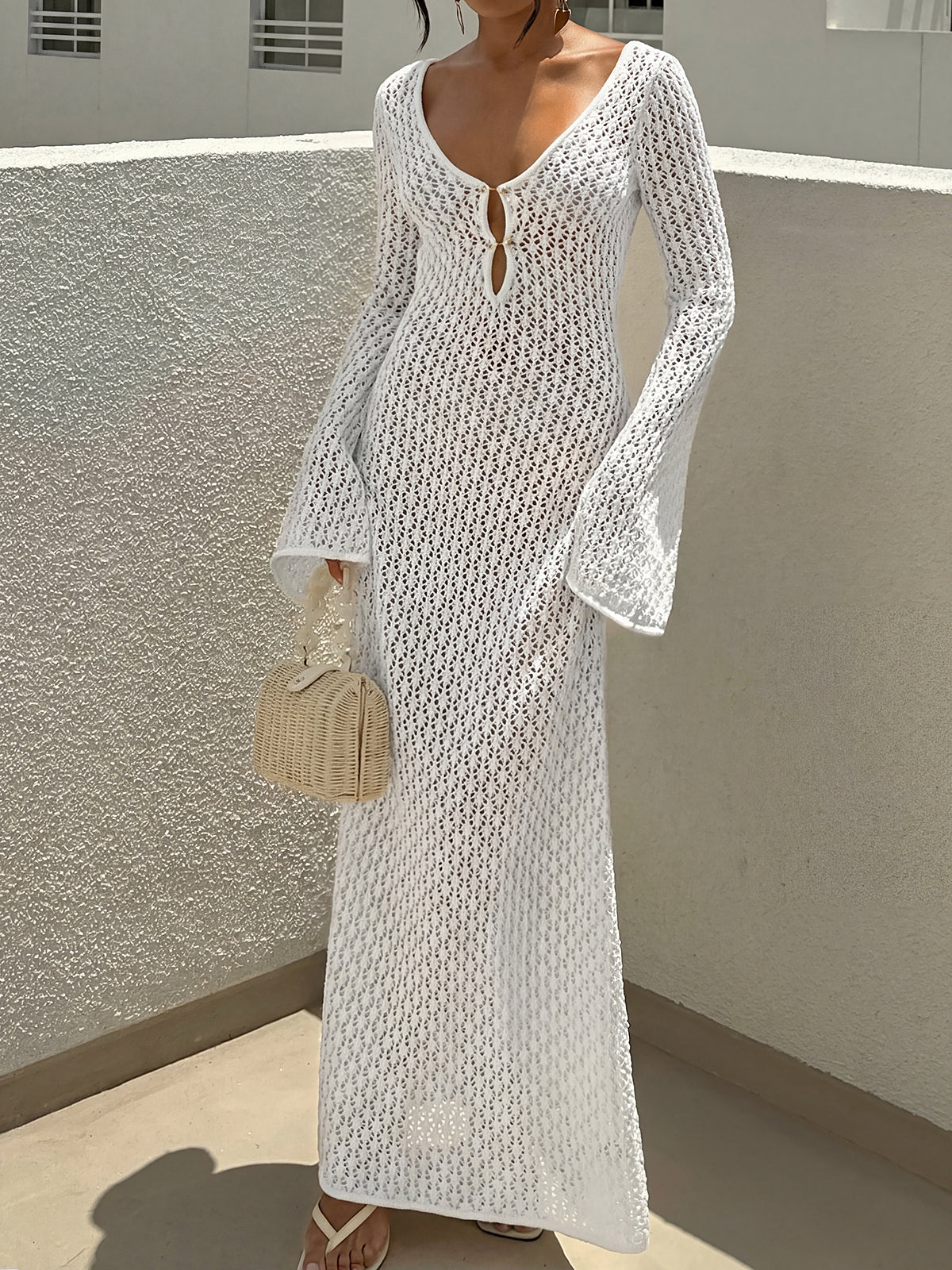 Woman wearing a white crocheted maxi dress with bell sleeves and a deep V-neckline.