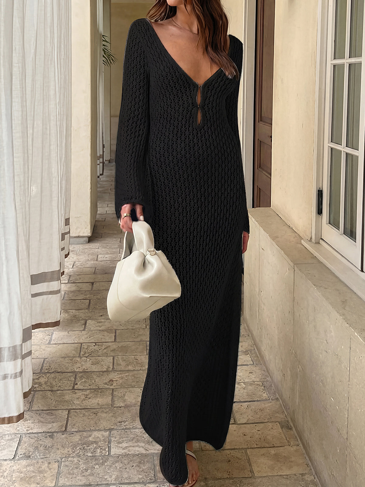 Woman wearing a black crocheted maxi dress with bell sleeves and a deep V-neckline, walking outdoors.
