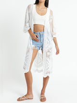 Woman wearing a white lace kimono over a white crop top and denim shorts