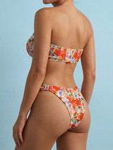 Rear view of a woman wearing an orange and pink floral print strapless bikini with ruched detailing on the bottoms.