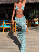 Woman wearing a blue and white floral print bikini with matching wide-leg sheer pants, standing on a wooden deck.