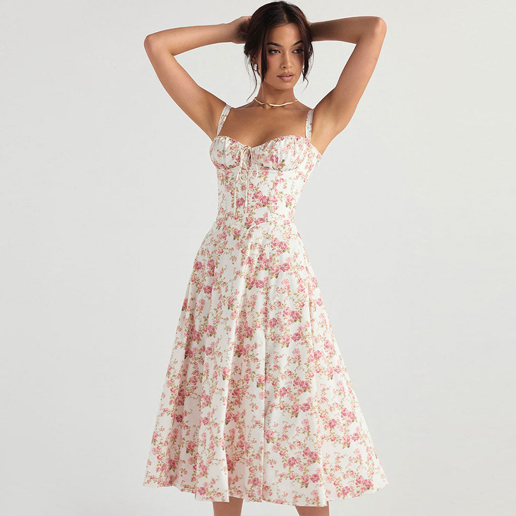 Woman wearing a white midi dress with a pink floral print and spaghetti straps, posing with hands behind her head.