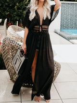 woman wearing a black sheer maxi cover-up with lace detailing at the waist and a plunging neckline, holding a patterned tote bag